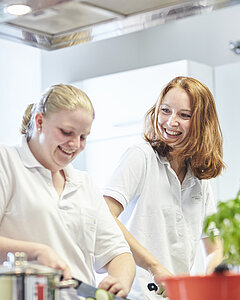 Zwei lächelnde Frauen kochen in der Lehrküche